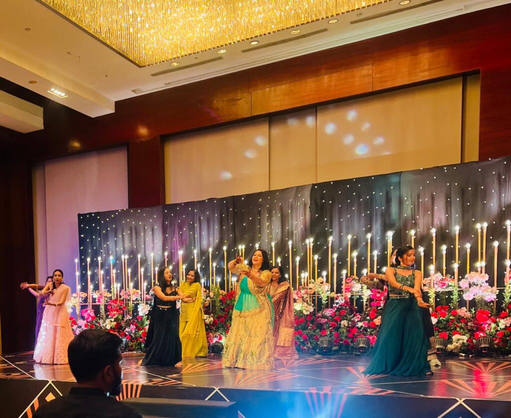 Women dancing on a decorated stage at a vibrant indoor event.